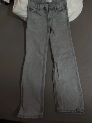 Gråa raka jeans med lågmidja - Säljer ett par gråa jeans med rak passform och låg midja. Jeansen har klassisk femficksdesign och är tillverkade i ett kraftigt denimtyg. Perfekta för en avslappnad och trendig look.