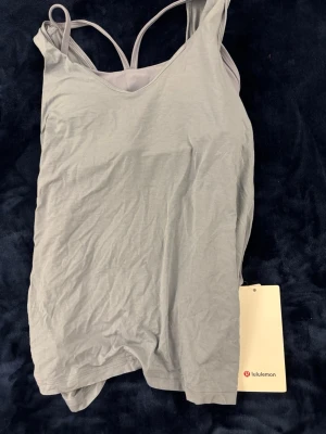 Helt ny lululemon sport linne med knytdetalj - Helt ny och använd med lappen fortfarande på. Den ser mer ljusblå ut i verkligheten och den är knytbar på baksidan så man kan justera lite men annars väldigt flowy och snygg.