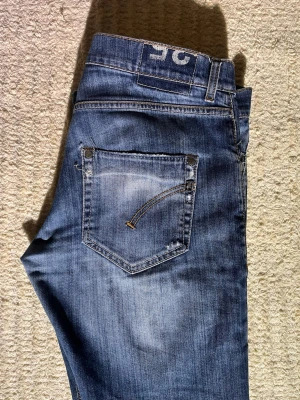 Blå jeans från Dondup med slitningar - Snygga blå jeans från Dondup med fina slitningar, storlek 35 vilket motsvarar ca 32:34.  Jeansen har lagats och har ett hål som ni kan se på bilden vi framfickan. Modellen är 186. Kom vid prisförslag!