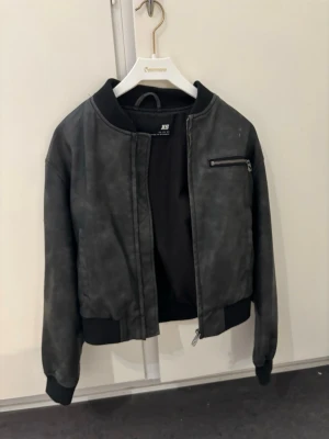 Svart bomberjacka i fejkskinn XS - Snygg svart bomberjacka från new Yorker i fejkskinn. Jackan har en klassisk bombermodell med ribbade muddar, dragkedja framtill och en cool bröstficka med dragkedja. Perfekt för dig som vill ha en stilren och edgy look.
