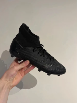 Adidas predator - Säljer ett par helsvarta fotbollsskor från Adidas med strumpkrage för extra stöd runt ankeln. Skorna har snörning och en texturerad ovandel i syntetmaterial för bättre bollkontroll. Perfekta för dig som vill ha stilrena och funktionella skor på planen.