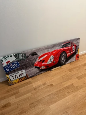 Tavla med röd sportbil och registreringsskyltar - Stor tavla med motiv av en klassisk röd sportbil och flera amerikanska registreringsskyltar. Tavlan har rektangulär form och tryckt motiv på canvas. Perfekt för dig som gillar bilar och vill ha något unikt på väggen.
