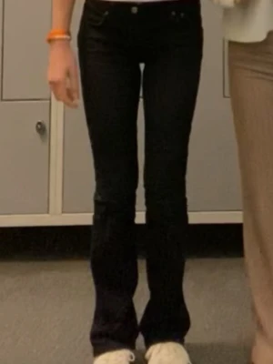 Svarta bootcut jeans med låg midja - Säljer ett par svarta bootcut jeans med låg midja och klassisk femficksdesign. Jeansen har en tight passform upptill och utsvängda ben nertill, vilket ger en snygg siluett. Perfekta för dig som gillar en trendig och avslappnad stil.