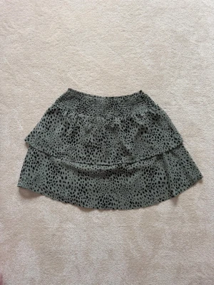 Grön kortkjol med leopardmönster - Snygg grön kortkjol med leopardmönster och volangdetalj. Kjolen har resår i midjan för skön passform och är perfekt för dig som vill sticka ut lite extra. 