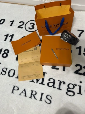 L och V Damier svart bälte - Säljer ett L och V bälte i klassiskt Damier-mönster i svart och grått med stor L och V-logga i silver på spännet. Bältet är gjort i skinn och har en exklusiv känsla, perfekt för att lyfta vilken outfit som helst.