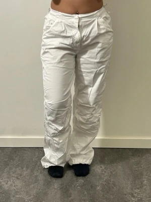 Vita loose parachute byxor med fickor - Säljer ett par vita loose parachute byxor med raka ben som går att justera i änderna och med fickor på sidorna. 