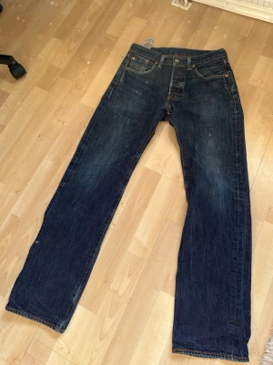 Levi's raka blå jeans - Klassiska blå jeans från Levi's med rak passform och fem fickor. Jeansen har en mörk tvätt med subtila slitningar och kontrastsömmar. Tillverkade i slitstark denim med den ikoniska röda Levi's-lappen på bakfickan. Perfekta för en avslappnad och tidlös stil.