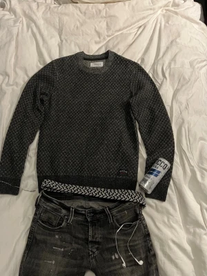 Mörkgrå stickad tröja - Snygg mörkgrå stickad tröja från Pier One med diskret mönster i vitt och svart. Tröjan har rund halsringning, ribbstickade muddar och en liten logotyp på nedre kanten. Perfekt för dig som gillar stilrena och bekväma plagg. Köpte för 500 kr nydligen, använt endast cirka 5 gånger. Liten i storleken.