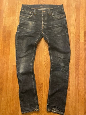 Nudie Jeans - Mörkblå jeans från Nudie Jeans med klassisk femficksdesign och mycket slitningar. Det är ett par slim jeans i modell Grim Tim. De är i strl W33 men passar mer som W30. Inga defekter. Mått på midja är 41,5, ytterbenslängd är 105 och benöppning är 16,8.