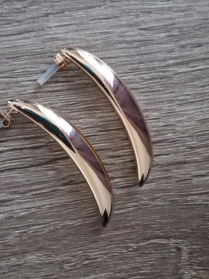 Guldiga böjda örhängen - Ett par långa, lätt rundade örhängen i plast med metallicskimrande yta. Längd 5,7 cm. Oanvända från HM