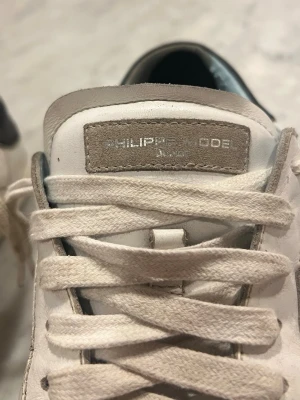 Vita sneakers från Philippe Model - Snygga vita sneakers från Philippe Model med klassisk design och beige detaljer. Skorna har snörning och en låg siluett. Ovandelen är i skinn och insidan har ljusblå detaljer. Perfekta för en stilren och avslappnad look. 