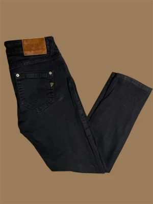 Svarta jeans från Dondup - Snygga svarta jeans från Dondup med klassisk femficksdesign och läderpatch bak i midjan. Jeansen har raka ben och diskreta detaljer på bakfickorna. Perfekta för en stilren och avslappnad look.