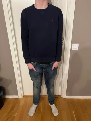 Mörk blå sweatshirt från Ralph lauren  -  De e barn storlek passar från runt 165-174 Mörkblå sweatshirt från Ralph Lauren med klassisk rund halsringning och den ikoniska röda logotypen broderad på bröstet. Tröjan har långa ärmar och ribbade muddar vid ärmslut och nederkant. Perfekt för en avslappnad och stilren look.