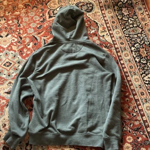 Mörkgrå hoodie från Pier One - Mysig mörkgrå hoodie från Pier One med huva och vita snören. Tröjan är i en skön blandning av polyester och bomull, perfekt för kyliga dagar. Klassisk passform med långa ärmar och ribbade muddar. Enkel och stilren design som funkar till det mesta.