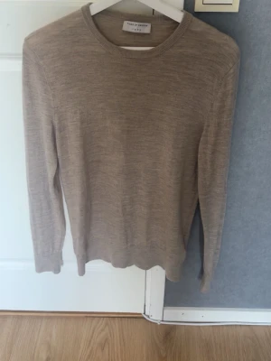 Beige stickad tröja Tiger of Sweden - Snygg beige stickad tröja från Tiger of Sweden med rund halsringning och långa ärmar. Tillverkad i ett tunt och mjukt material som passar perfekt till lager-på-lager. Klassisk och stilren design utan huva.