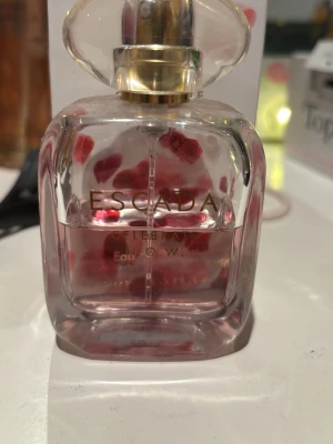 Escada Celebrate N.O.W. EdP 50ml - Escada Celebrate N.O.W. Eau de Parfum i en elegant glasflaska med gulddetaljer. Doften kommer i en söt förpackning dekorerad med rosa och vita hjärtan. Parfymen har en feminin och fräsch känsla, perfekt för dig som gillar blommiga och fruktiga toner. Köpt för cirka 800, endast hälften kvar men luktar otroligt gott