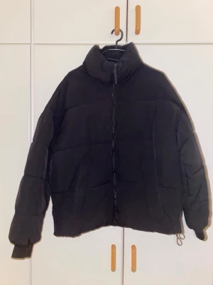 Svart pufferjacka från Bershka - Säljer en svart pufferjacka från Bershka i storlek XS. Jackan har hög krage, dragkedja framtill och en boxig, trendig passform. Perfekt för kalla vinterdagar och enkel att matcha med olika outfits. Materialet är syntetiskt och håller värmen bra.