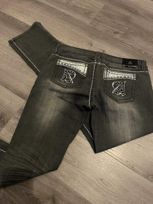 Svarta jeans med slitningar, Lågmidjade - Snygga svarta jeans från  Antique Rivet med vita kontrastsömmar och slitna detaljer på låren. Klassisk femficksmodell och raka ben. Perfekta för en cool och avslappnad stil. Lågmidjade