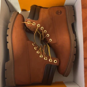 Bruna Timberland kängor i läder - Säljer ett par klassiska bruna Timberland kängor i nubuckläder med robust sula och guldfärgade metallhål för snörningen. Kängorna har vadderad brun krage och ikoniska loggan på sidan. Perfekta för kalla dagar och snygga till jeans eller cargo.