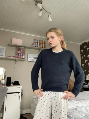 Mörkblå stickad tröja med rund hals - En enkel och stilren mörkblå stickad tröja med rund hals och långa ärmar. Tröjan har en rak passform och ribbstickade muddar vid ärmslut och nederkant. Perfekt för att hålla sig varm under kyliga dagar.