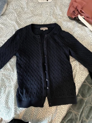 Mörblå kofta - Mörkblå kabelstickad kofta från Basic you i ekologisk bomull. Koftan har rund hals, knappar framtill och ribbade muddar vid ärmslut och nederkant. Köpt för nåt år sedan men nästan aldrig använd.