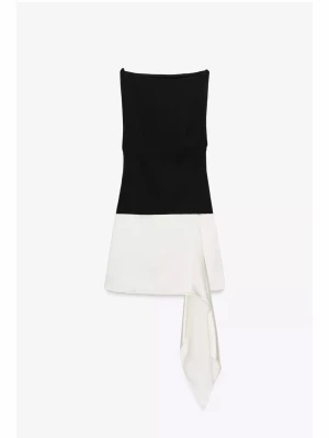 Svartvit axelbandslös kort klänning - Snygg svartvit axelbandslös kort klänning med rak överdel och asymmetrisk detalj i kjolen. Klänningen har en elegant tvåfärgad design och en dekorativ slits med tygdetalj framtill. Perfekt för dig som gillar stilrena kontraster.
