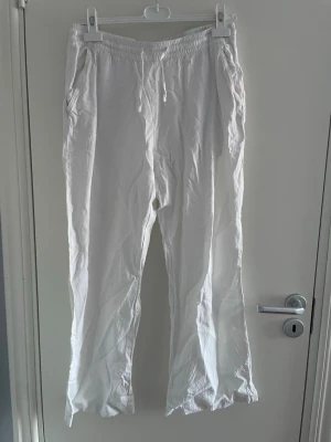 Vita linnebyxor med dragsko - Säljer ett par vita linnebyxor med avslappnad passform och resår i midjan samt dragsko. Byxorna har sidofickor och är tillverkade i ett lätt och luftigt linnematerial, perfekta för en chill och stilren look.