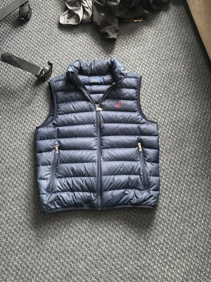 Mörkblå dunväst från Polo Ralph Lauren - Mörk blå polo Ralph lauren väst. Storlek M. Modellen på bilden är 184. Skulle rekommendera att va ungefär 180/178. Mycket bra skick 