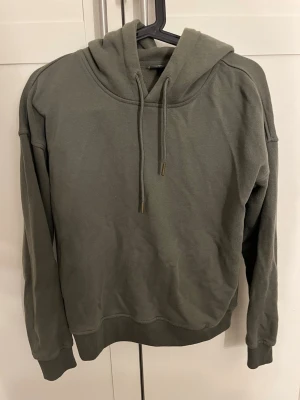 Olivgrön hoodie från Urban Classics - Säljer en olivgrön hoodie från Urban Classics i storlek S. Hoodien har en klassisk passform med huva och dragsnören samt ribbade muddar vid ärmslut och nederkant. Perfekt för en chill och avslappnad stil.