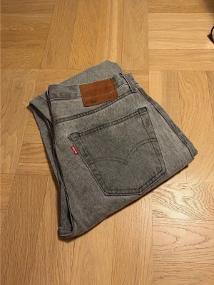 Grå Levi's 501 jeans 30/32 (Mindre slitningar)  - Säljer ett par klassiska grå Levi's 501 jeans med rak passform och fem fickor. Jeansen har storlek W 30 och L 32 och snygg röd Levi's-tag på bakfickan. Tillverkade i slitstark denim, perfekta för en avslappnad och tidlös stil. Defekt på jeansen längst ner (kan ses i näst sista bild), samt väldigt litet hål i skrevet men inget som märks (sista bild) 