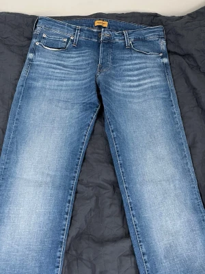 Blå slim jeans från jack&jones - Snygga blå slim jeans från jack& jonesmed klassisk femficksmodell och slitningar framtill. Jeansen har en tvättad look och är tillverkade i stretchigt denim för extra komfort. Perfekta för dig som gillar en smal passform och stilren design.