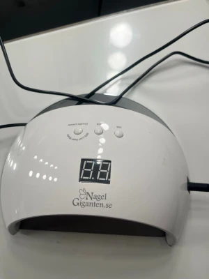 UV-lampa från Nagelgiganten - Den populära UV-lampan från Nagelgiganten i vit plast. Den har några repor på metallplattan men det är inget som påverkar funktionen, den fungerar perfekt! Är superbra för att härda gelélack och andra nagelprodukter. Lampan har en halvmåneformad design och ansluts med strömadapter.