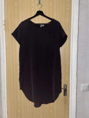 Svart t-shirtklänning från H&M Divided - Enkel svart t-shirtklänning från H&M Divided med rund halsringning och korta ärmar. Rak och avslappnad passform i mjukt bomullsmaterial. Perfekt basplagg att styla med sneakers eller boots.
