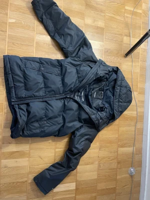 Svart jacka från tre torn storlek S - Snygg svart jacka från Tre torn med huva och dragkedja framtill. Jackan är i storlek S men passar även M. Jackan har två snedställda fickor med knappar och quiltad design. Perfekt för kalla vinterdagar och riktigt skön att bära.