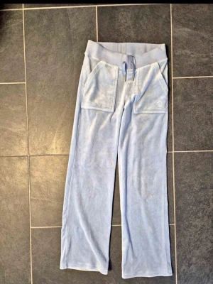 Ljusblå byxor Juicy Couture - Säljer ett par ljusblå mjukisbyxor från Juicy Couture i mjuk velour. Byxorna har raka ben, bred resår i midjan med dragsko, stora fickor fram och bakfickor med knapp. Perfekta för en chill och trendig look. Köpta för 1200kr. Pris kan diskuteras 