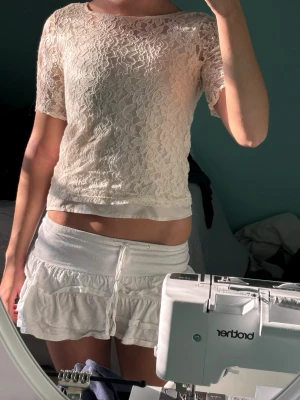 Vit spetsblus med kort ärm - Säljer en söt vit blus i spets med korta ärmar och rund hals. Toppen är lätt croppad och har ett romantiskt blommönster i spetsmaterial som ger en fräsch och somrig vibe. Perfekt att styla med kjol eller jeans för en trendig look.