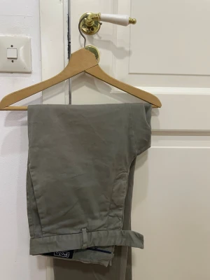 Vintage Grå tygbyxor från Polo Ralph Lauren - Ett par otroligt snygga grå tygbyoxor från Polo Ralph Lauren, med en  klassisk passform och stilrena detaljer som bruna knappar och bälteshällor. Materialet är mjuk bomull och insidan har märkets signaturband. 