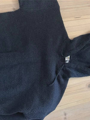 Svart teddyhoodie från Gina Tricot - Mysig svart hoodie från Gina Tricot i teddy-material. Hoodien har en stor huva och dragsko, samt en klassisk känguruficka framtill. Perfekt för dig som gillar en chill och avslappnad stil. Materialet är fluffigt och ger en skön vibe.