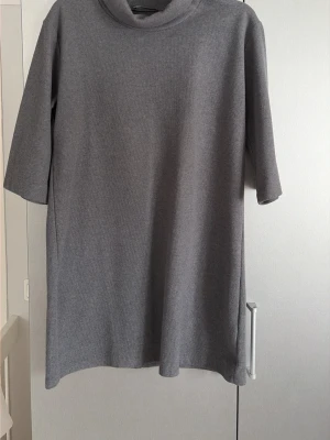 Grå stickad klänning från Trendyol - Säljer en enkel och stilren grå stickad klänning från Trendyol. Tröjan har halvpolo, raka trekvartsärmar och är gjord i mjukt stickat material.