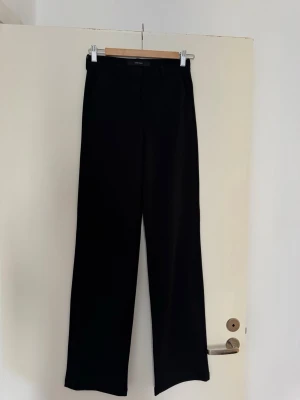 Svarta kostymbyxor från Vero Moda - Säljer ett par svarta kostymbyxor från Vero Moda i storlek XS/34. Byxorna har raka ben och hög midja, vilket ger en clean och stilren look. Perfekta för dig som gillar minimalistisk stil. Materialet känns mjukt och följsamt.