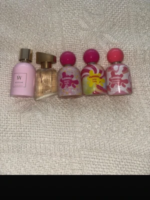 Mix av parfymflaskor i rosa toner - Säljer ett set med fem parfymflaskor i olika former och färger. Inkluderar en ljusrosa W Azúcar-flaska med guldfärgat lock, en transparent flaska med guldlock samt tre TUBEREE-flaskor i rosa, gult och vitt med färgglada etiketter och runda lock.