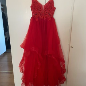 Röd balklänning med spetsdetaljer - Säljer en röd långklänning med tunna axelband och v-ringning. Överdelen har vackra spetsdetaljer och kjolen är i flera lager av luftig tyll som ger en voluminös känsla. Perfekt för bal eller festliga tillfällen. Köptes för 2500kr men säljs nu för 1000kr❣️Skriv gärna om du vill ha en bild hur den ser ut på 💕