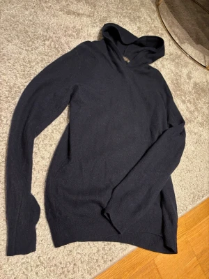 Mörkblå hoodie från Oscar Jacobson - Snygg mörkblå hoodie från Oscar Jacobson i mjukt och tunt material. Klassisk design med huva och långa ärmar, perfekt för en avslappnad och stilren look. Passar lika bra till jeans som till mjukisbyxor.