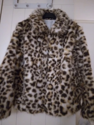 HELT NY & OANVÄND snygg Leopardmönstrad fusk pälsjacka,  faux fur, Large - HELT NY & OANVÄND supersnygg mjuk/len leopardmönstrad fuskpälsjacka med krage och långa ärmar, storlek Large. Fickor. Satinfoder. Stängs med hakar. Helt felfri. Jackan har en cool och trendig look med svart, beige och bruna toner. Perfekt för dig som vill sticka ut och hålla dig varm under vintern. Slutsåld online och finns ej i fysisk butik.