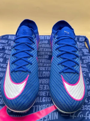 Nike Mercurial Vapor 16 Elite FG - Attack  - Snygga Nike Mercurial fotbollsskor i blått med vita och rosa detaljer. Skorna har en strömlinjeformad design, syntetiskt material och tydliga Nike-loggor på sidan och hälen. Perfekta för snabba vändningar på planen och grym kontroll på bollen.