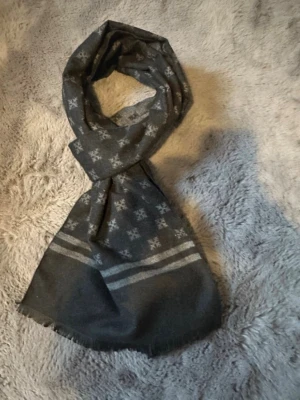 Mörkgrå/grå halsduk med mönster - Snygg mörkgrå och grå halsduk med diskret geometriskt mönster i ljusgrått. Halsduken har tunna fransar i kanterna. Har aldrig använts.