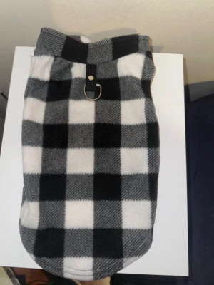 Rutig fleecejacka till katt/hund - Säljer en svartvit rutig fleecejacka för hund eller katt med D-ring i metall på ryggen för koppel. Jackan har hål för frambenen och är gjord i mjukt fleece-material. Den passar vanliga katter eller mindre hundar. Har bara testat en gång