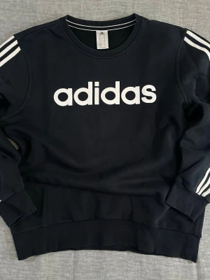 Adidas Spell Out Crewneck Black – Oversized Streetwear 90’s style  - Classic black Adidas crewneck with bold white spell-out logo and iconic three stripes down sleeves. Clean sporty silhouette with relaxed oversized fit. Perfect with cargos, denim or biker shorts. Easy everyday streetwear piece with strong athletic vibe.  Good used condition. No major flaws.