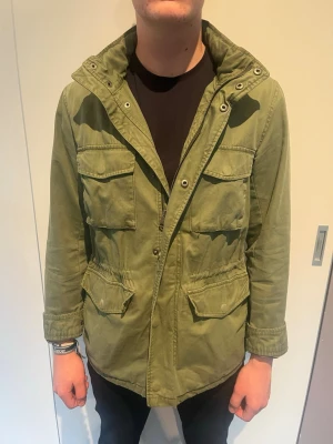 Grön parkajacka med fickor - Snygg grön parkajacka med fyra stora fickor framtill och hög krage. Jackan har knapp- och dragkedjestängning samt en avslappnad passform. Perfekt för lager på lager och streetwear-vibe. Passar M perfekt