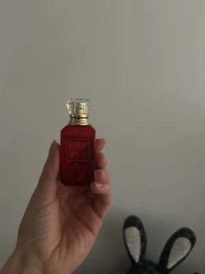 Kayali JUICY Apple parfym    - Snygg parfym från Kayali i en lyxig röd glasflaska med gulddetaljer och en kristalliknande kork. Flaskan har en elegant, geometrisk form och texten 'KAYALI' i guld på framsidan. Perfekt för dig som gillar exklusiva dofter och snygg design.